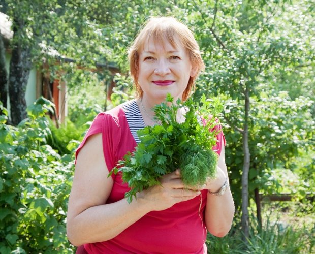 Женщина в огороде держит в руках зелень