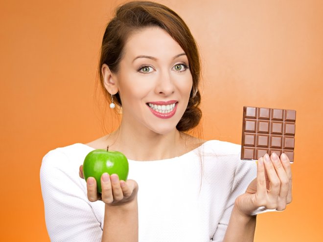 женщина держит шоколадку и яблоко