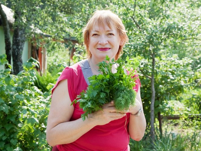 Женщина в огороде держит в руках зелень